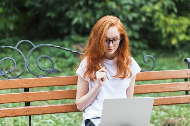 Woman on bench with laptop and pen