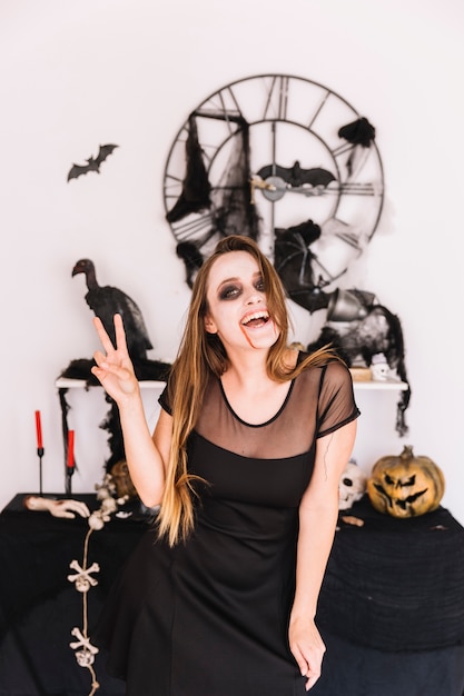 Free photo woman in black dress in front of halloween composition smiling and showing peace