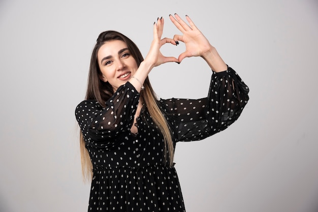 Woman in black dress giving heart sign.