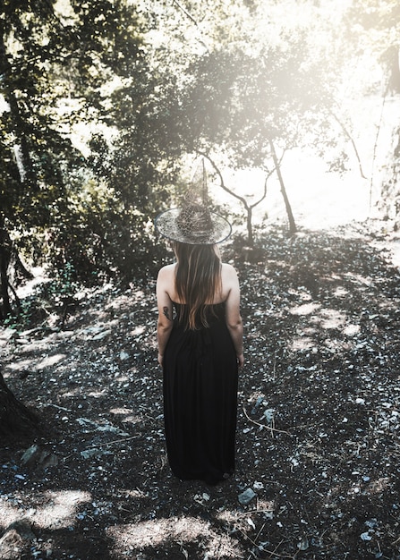 Free photo woman in black dress and hat standing in forest