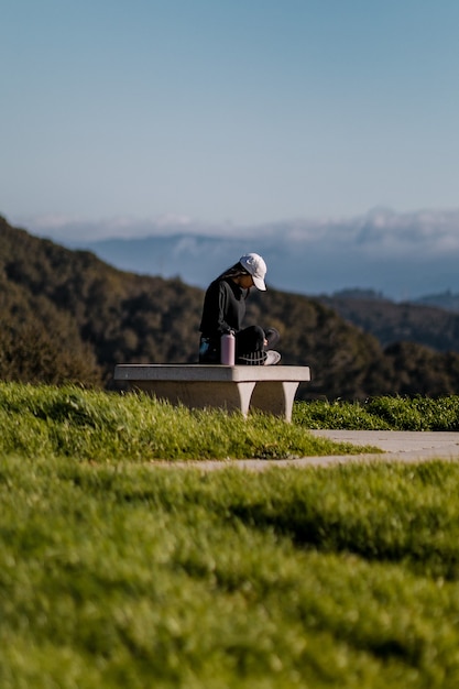 Woman in black jacket sitting on gray concrete bench during daytime