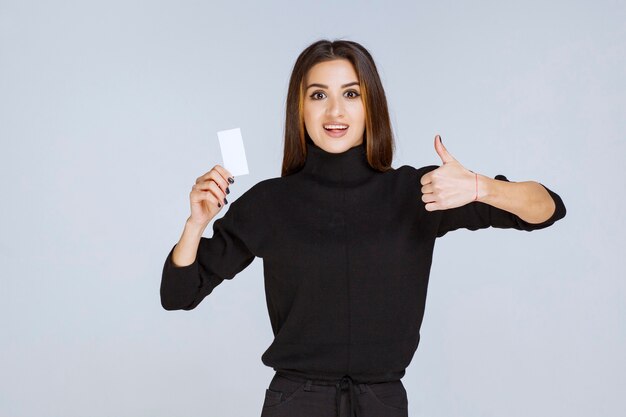 woman in black shirt showing her business card and looks satisfied. 