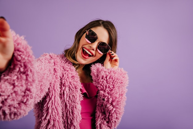 Free photo woman in black sunglasses posing on purple wall