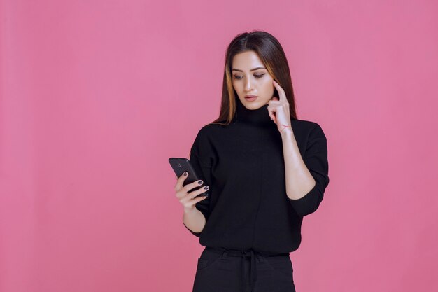 Woman in black sweater holding a smartphone and texting or checking social media. 