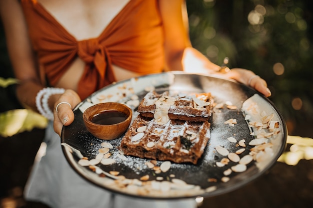 Free Photo woman in brown bra holds plate with waffles, chocolate sauce and peanuts