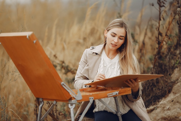 Free photo woman in a brown coat painting in a field