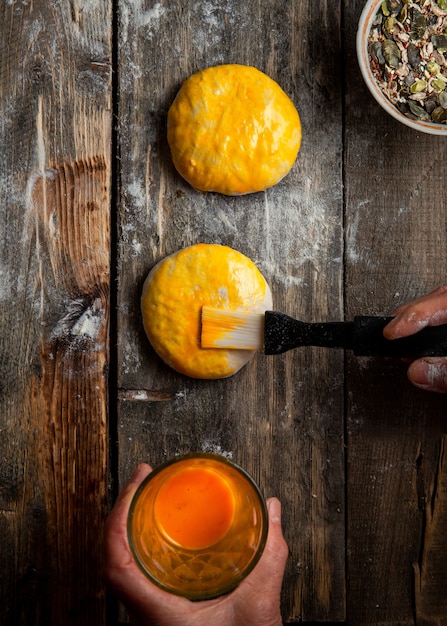 Woman brushing dough with egg yolk before baking top view