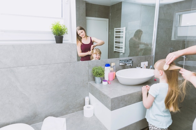 Free photo woman brushing girl near mirror