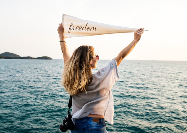 Free photo woman by the sea holding flag with freedom inscription