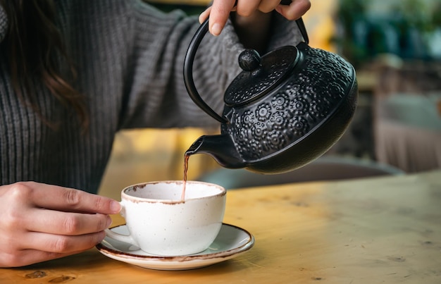 Woman in a cafe pour tea from a black cast iron teapot