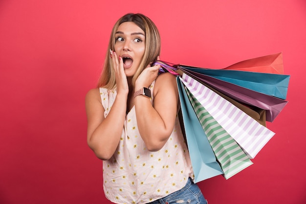 Free Photo woman carrying shopping bags while covering her face on red wall . 