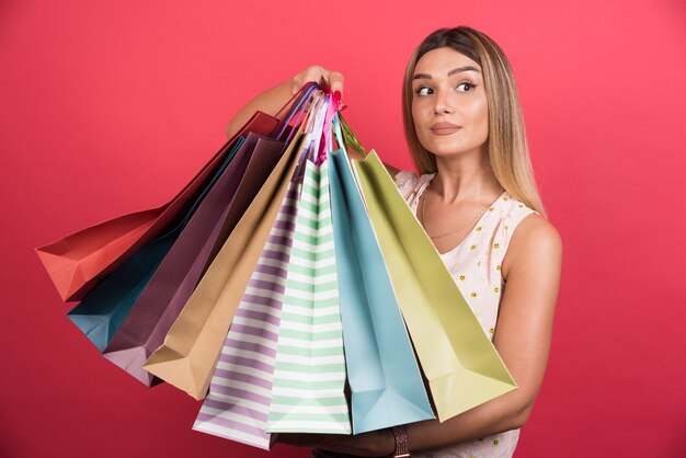 Woman carrying shopping bags with neutral expression on red wall . 