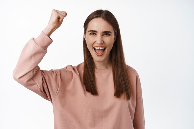 woman chanting, rooting for team. Girl activist raising her fist fighting equality, fist pump, looks encouraged and determined, standing on white.