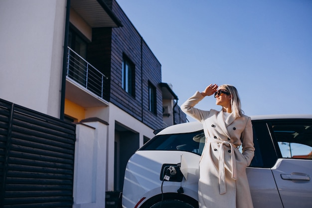 Free photo woman charging electro car by her house