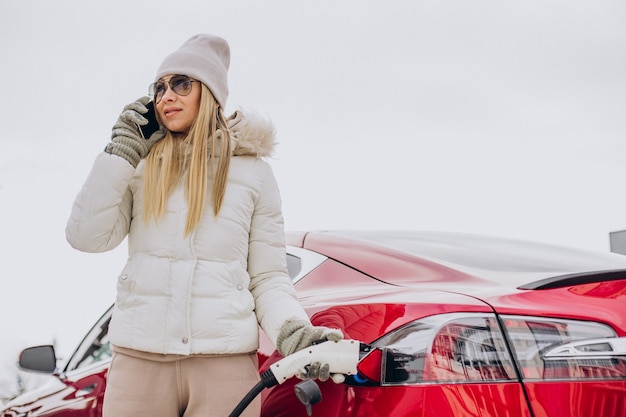 Woman charging red electro car, in winter time