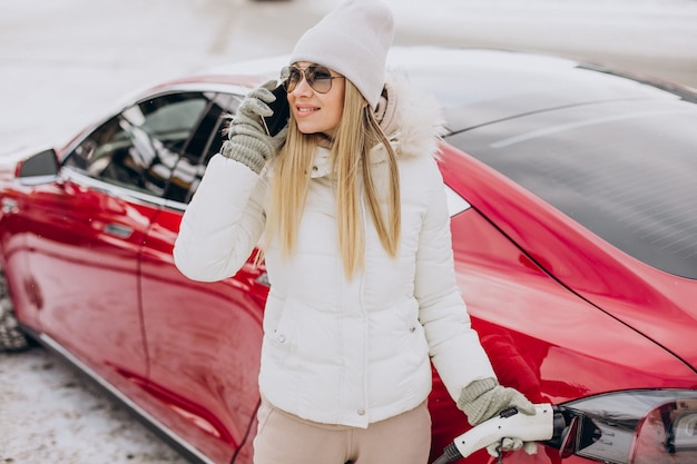 Woman charging red electro car, in winter time