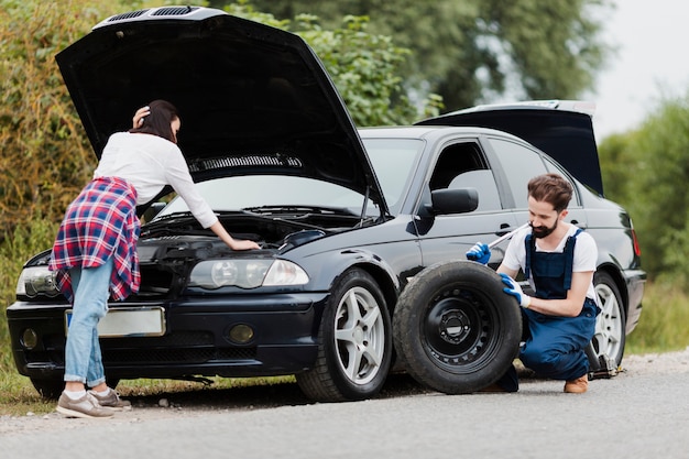 Free Photo woman checking engine and man changing tyre