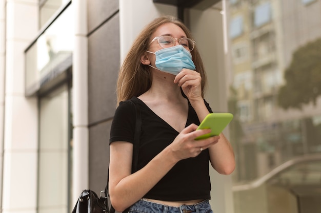 Woman checking her phone while wearing a medical mask outdoors