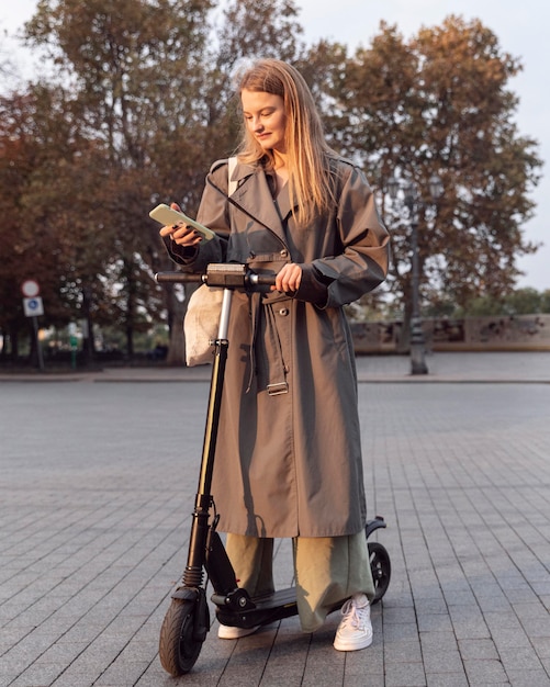 Free photo woman checking her smartphone while on electric scooter outdoors