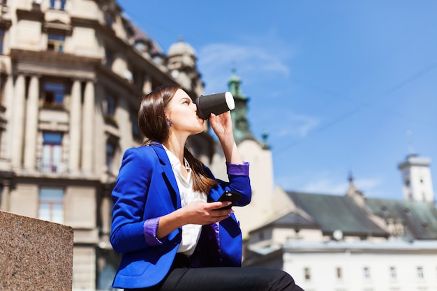 Free photo woman checks her phone sitting with cup of coffee on the street