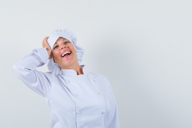 woman chef holding hand on head in white uniform and looking cheerful.