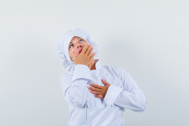 woman chef holding hand on mouth in white uniform and looking surprised