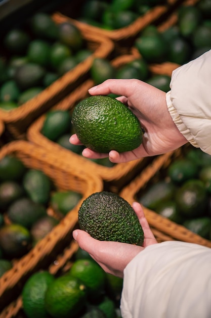 A woman chooses an avocado in a grocery store