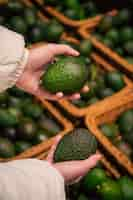 Free photo a woman chooses an avocado in a grocery store