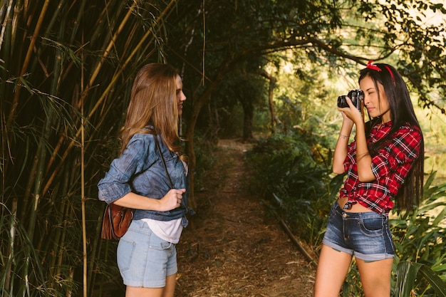 Woman clicking her friend's photograph with camera in forest