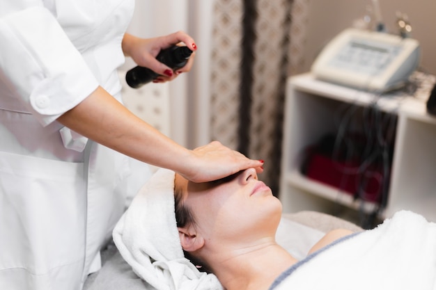 Woman client in salon receiving manual facial massage from beautician