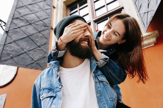 Woman closes her man's eyes while he holds her on his back