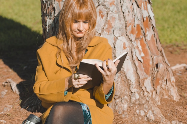 Woman in coat reading under tree