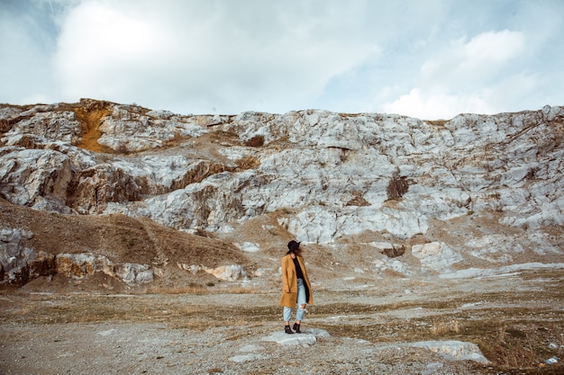 Woman in a coat standing in the rocky mountains on an autumn day