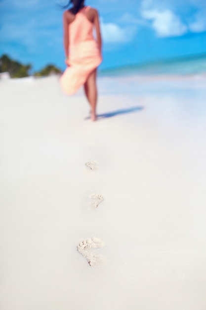 Free photo woman in colorful dress walking on beach ocean leaving footprints in the sand