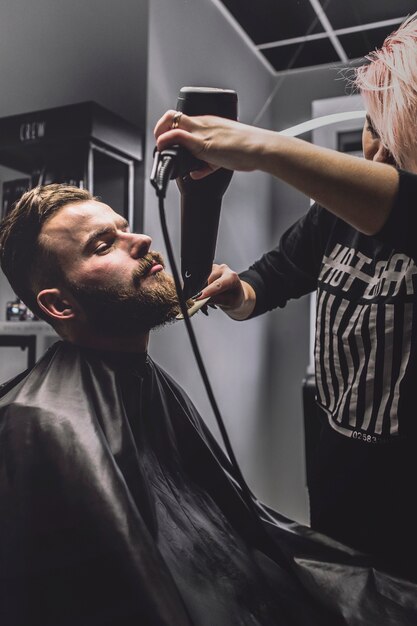 Woman combing and drying beard of client