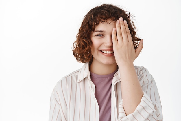 Free photo woman coning half of face with palm, smiling happy, checking vision in optician store or showing before and after effect, standing on white