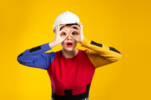 Woman in construction helmet shows glasses with fingers