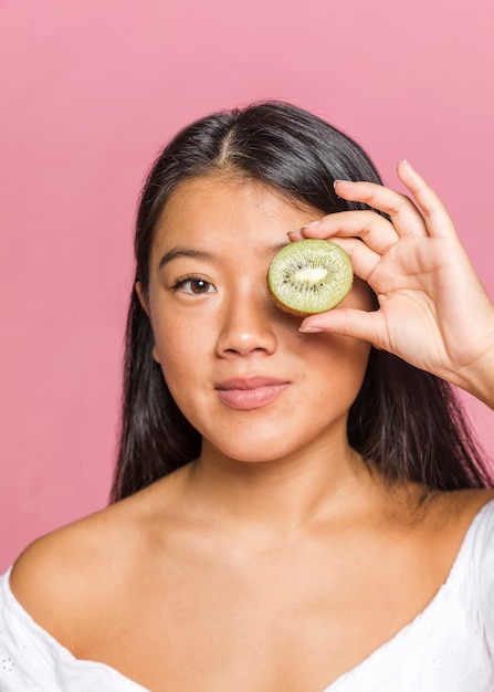 Woman covering her eye with kiwi and looking at camera