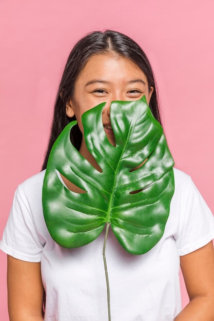 Free photo woman covering her face with monstera leaf