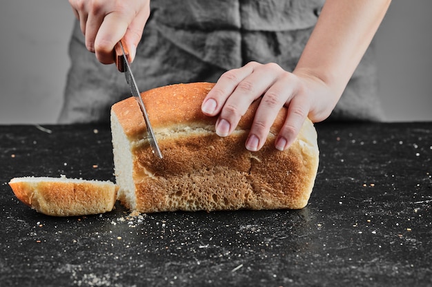 Free photo woman cutting bread with knife on dark desk.