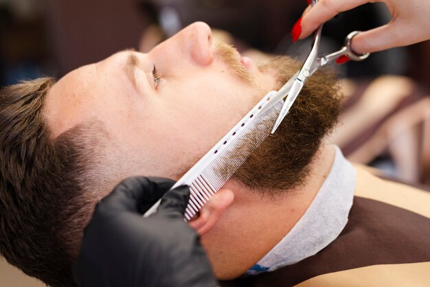 Woman cutting a client's beard close-up