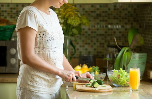 Free Photo woman cutting cucumbers for a salad on the kitchen