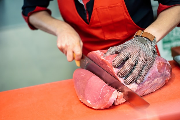 Free photo woman cutting fresh meat in a butcher shop with metal safety mesh glove