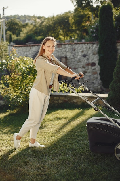 Free photo woman cutting grass with lawn mover in the back yard. lady on a grass.