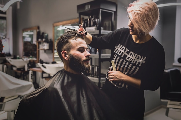 Woman cutting hair of man in salon