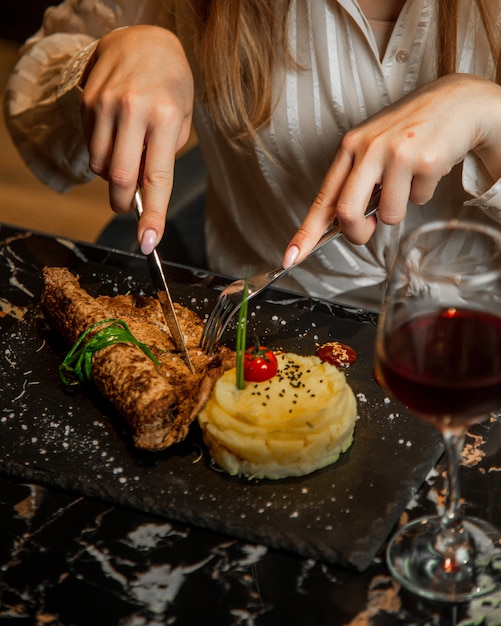 Free photo woman cutting meat steak with masked potato and glass of red wine.