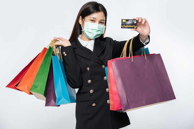 A woman in dark and wearing a mask walks shopping, carries credit cards, and lots of bags