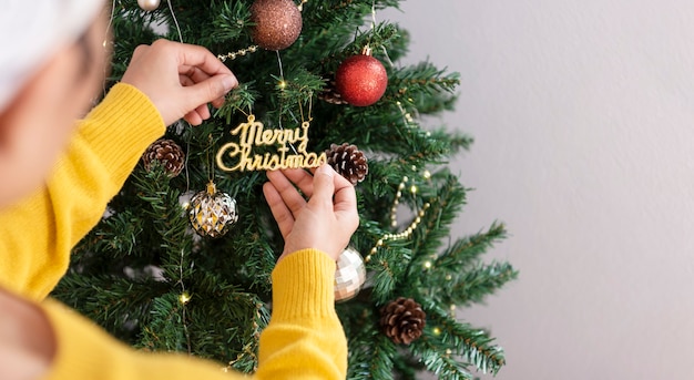 Woman decorating a Christmas tree with ornaments in christmas day.