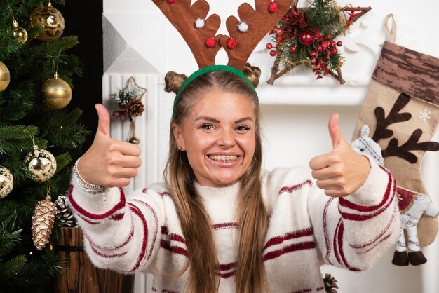 Woman in deer ears sitting on carpet and giving thumbs up.