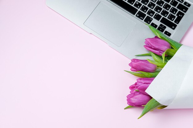 Woman desktop with Laptop and violet tulips on pink background Flat lay Spring holiday Mother day